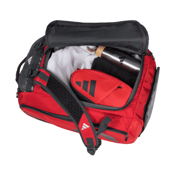 Die farbenfrohe Adidas Tour 3.3 Solar Rot Padeltasche ist geöffnet und präsentiert ihren Inhalt: ein weißes Hemd, eine schwarze Hose, eine rote, mit dem Logo verzierte Tasche und eine silberne Metallwasserflasche. Diese Tasche ist auf Funktionalität ausgelegt und verfügt über mehrere Fächer und einen gepolsterten Riemen. Sie kombiniert mühelos Stil und Funktionalität.