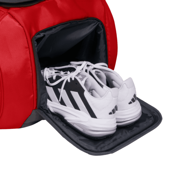 Ein Paar Sportschuhe im eleganten weiß-schwarzen Design liegen ordentlich im Schuhfach einer Adidas Tour 3.3 Solar Rot Padeltasche, wobei das Fach geöffnet ist, um ihren makellosen Zustand zu präsentieren.