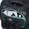 Eine Adidas Tour Anthrazit 2024 Padeltasche in Schwarz und Blaugrün mit einer teilweise geöffneten Vordertasche offenbart ein gefaltetes Handtuch mit Sportlogo und eine graue Wasserflasche im Inneren. Dieser Rucksack wurde für Ihre nächste Tour entworfen und verfügt über einen Tragegriff und verstellbare Riemen.