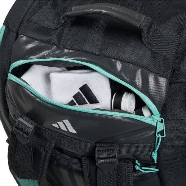 Eine Adidas Tour Anthrazit 2024 Padeltasche in Schwarz und Blaugrün mit einer teilweise geöffneten Vordertasche offenbart ein gefaltetes Handtuch mit Sportlogo und eine graue Wasserflasche im Inneren. Dieser Rucksack wurde für Ihre nächste Tour entworfen und verfügt über einen Tragegriff und verstellbare Riemen.