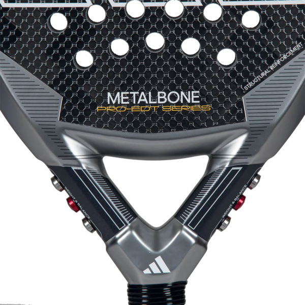 Eine Detailansicht des Adidas Metalbone Pro EDT 2024 Paddle-Schlägers hebt seine strukturierte Oberfläche mit sechseckigen Löchern hervor, ergänzt durch elegante Designelemente in Schwarz und Grau.