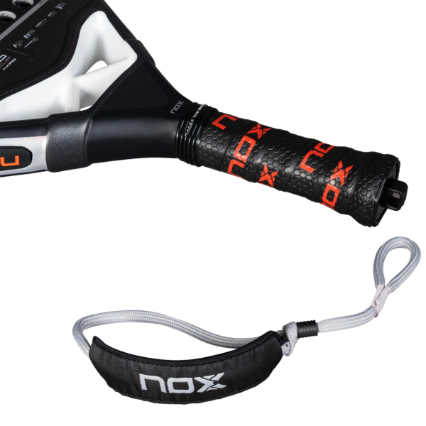 Nahaufnahme eines schwarz-weißen NOX AT10 Pro Cup HARD 2025 Padelschlägergriffs mit strukturiertem Griff und dem Markennamen „NOX“ in Rot und Weiß. Anbei eine graue Handschlaufe mit schwarzem Pad, die ebenfalls das „NOX“-Logo trägt.